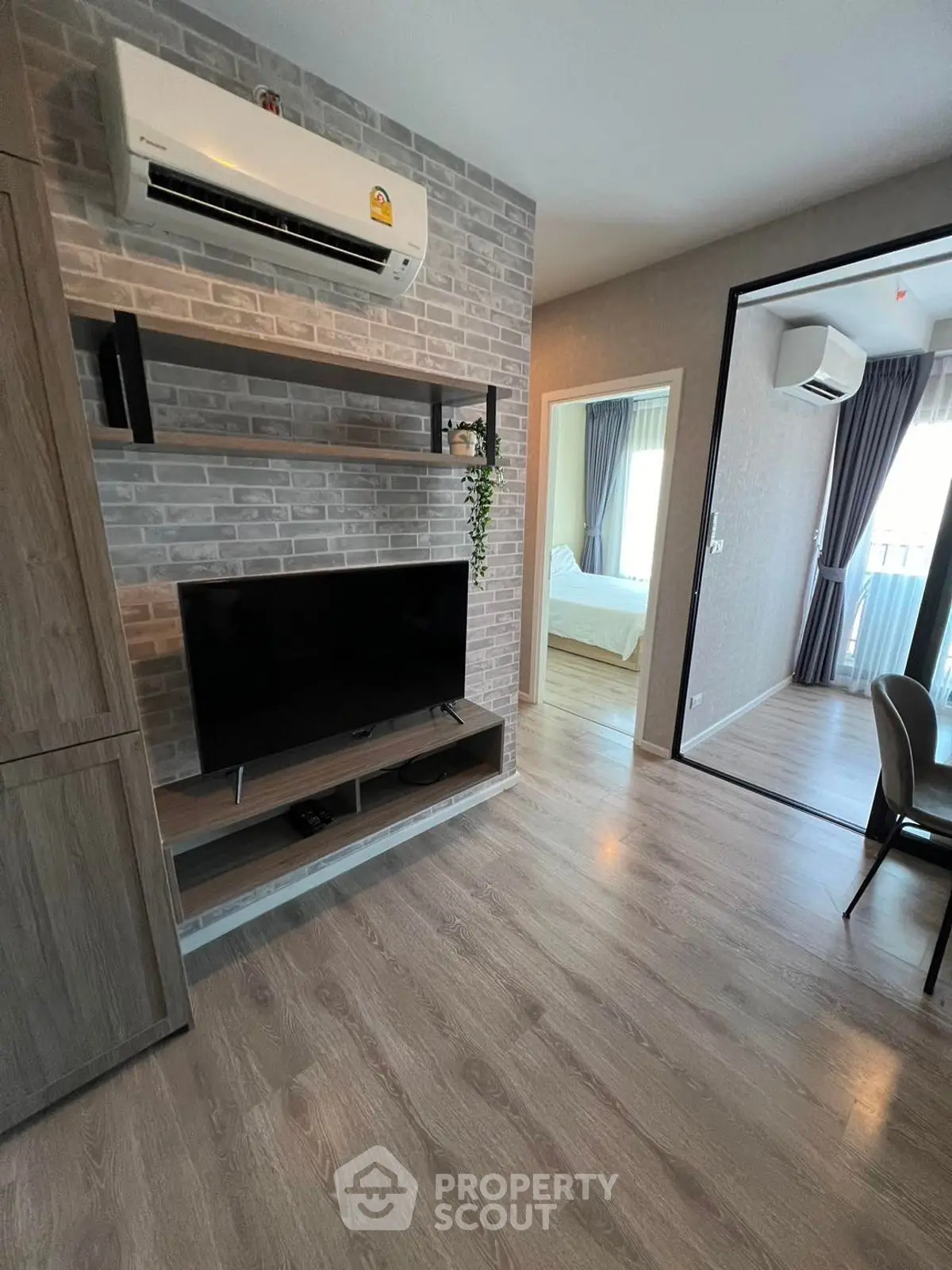 Modern living room with TV and air conditioning, open view to bedroom, stylish wood flooring.