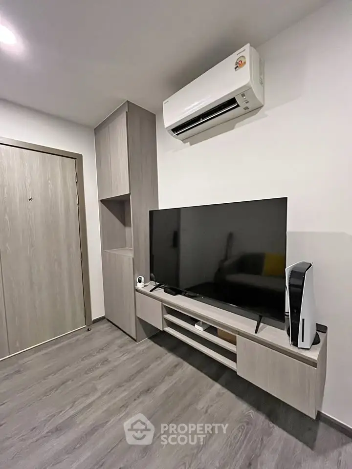 Modern living room with sleek TV setup and air conditioning, featuring stylish wood flooring and built-in storage.