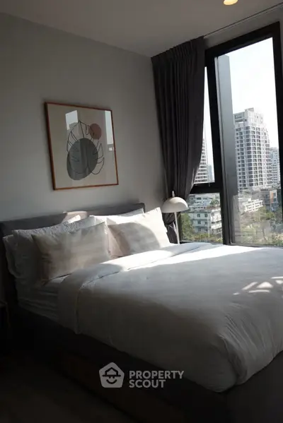 Modern bedroom with large window offering city view, stylish decor, and cozy bedding.
