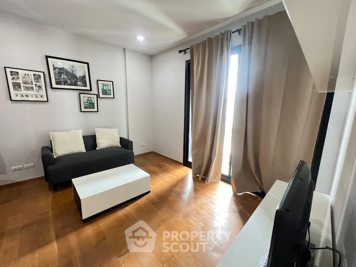 Modern living room with hardwood floors, cozy sofa, and large window with curtains.