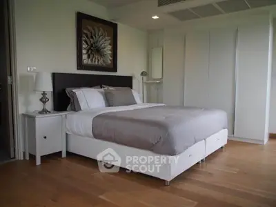 Spacious bedroom with modern decor and hardwood floors, featuring a comfortable bed and stylish artwork.