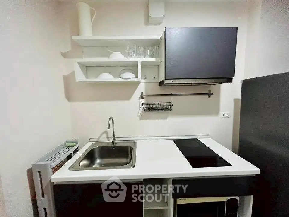 Compact modern kitchen with sleek black cabinets and open shelving, featuring an electric cooktop and stainless steel sink.