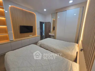 Modern bedroom with twin beds and ambient lighting, featuring sleek built-in storage and a wall-mounted TV.