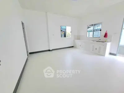 Spacious unfurnished room with white walls and tiled floor, featuring a small kitchenette area.