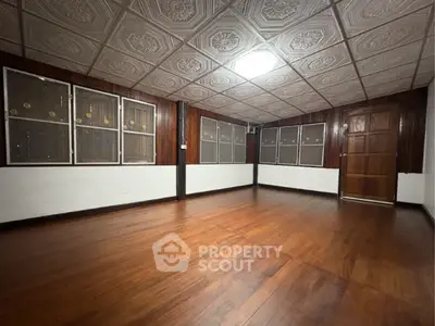 Spacious empty room with wooden flooring and decorative ceiling tiles