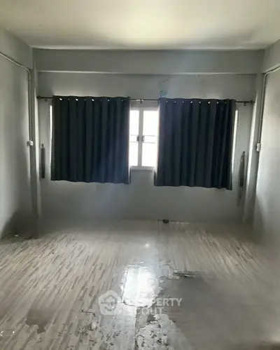 Spacious empty room with tiled flooring and large window with curtains.