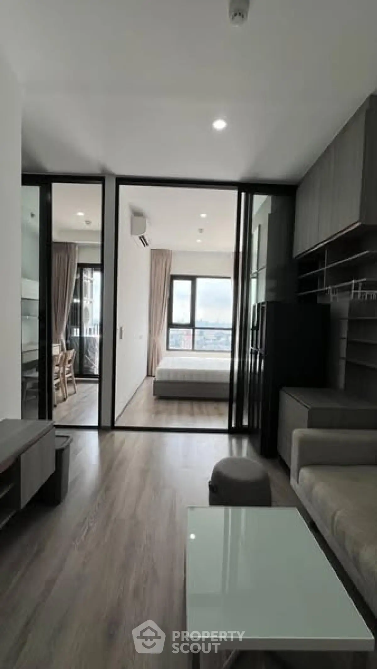 Modern apartment interior with open living room and bedroom, featuring sleek design and large windows.