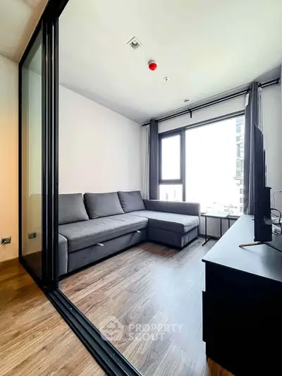Modern living room with sleek gray sofa and large window offering city views.