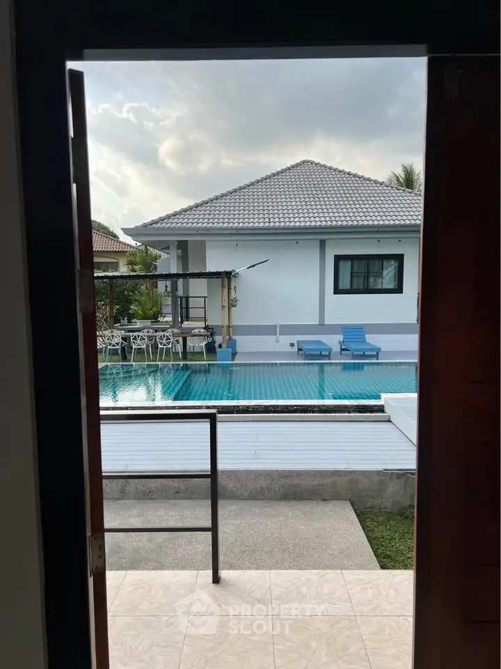 Charming villa with pool view from doorway, featuring outdoor seating and modern architecture.