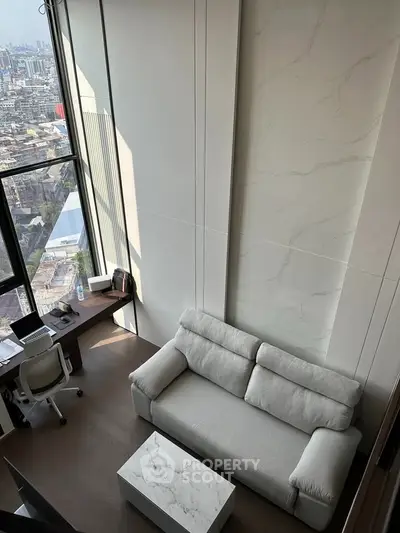 Modern living room with high ceilings and city view, featuring a cozy sofa and workspace.