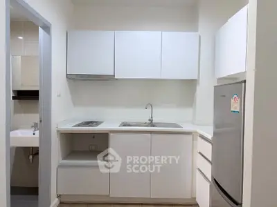 Modern compact kitchen with sleek white cabinets and stainless steel fridge in a cozy apartment.