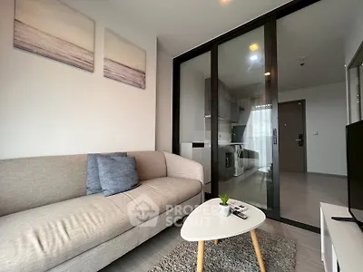 Modern living room with cozy sofa and sliding glass doors leading to a sleek kitchen.