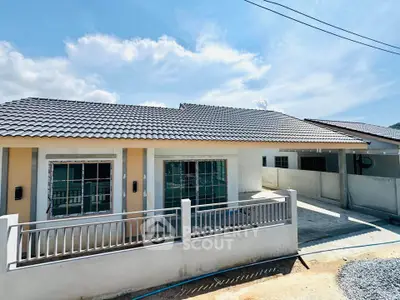 Charming single-story house with tiled roof and fenced yard under a clear blue sky.