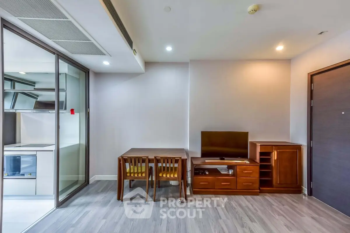 Modern apartment interior with open kitchen and dining area, featuring sleek furniture and bright lighting.