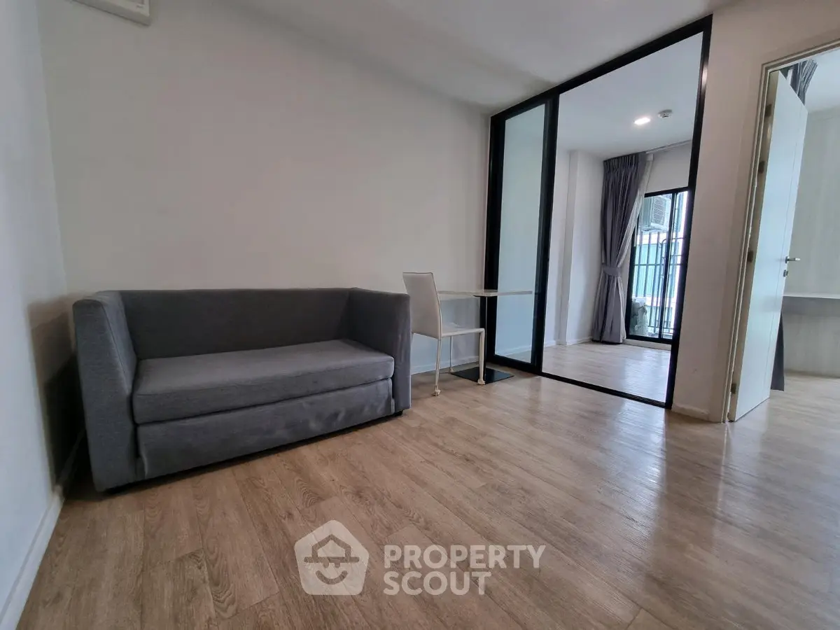 Modern living room with sleek gray sofa and glass partition leading to balcony.