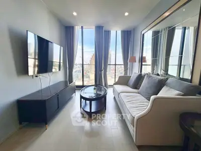 Modern living room with large windows and city view, featuring a sleek sofa and wall-mounted TV.