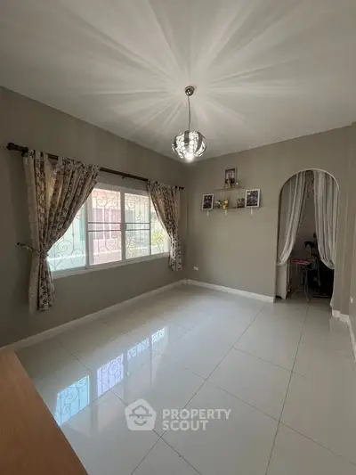 Spacious living room with elegant chandelier and large window, perfect for natural light.