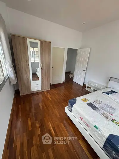 Spacious bedroom with wooden flooring and modern wardrobe in a bright apartment.