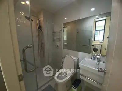 Modern bathroom with glass shower, toilet, and washing machine in sleek apartment.