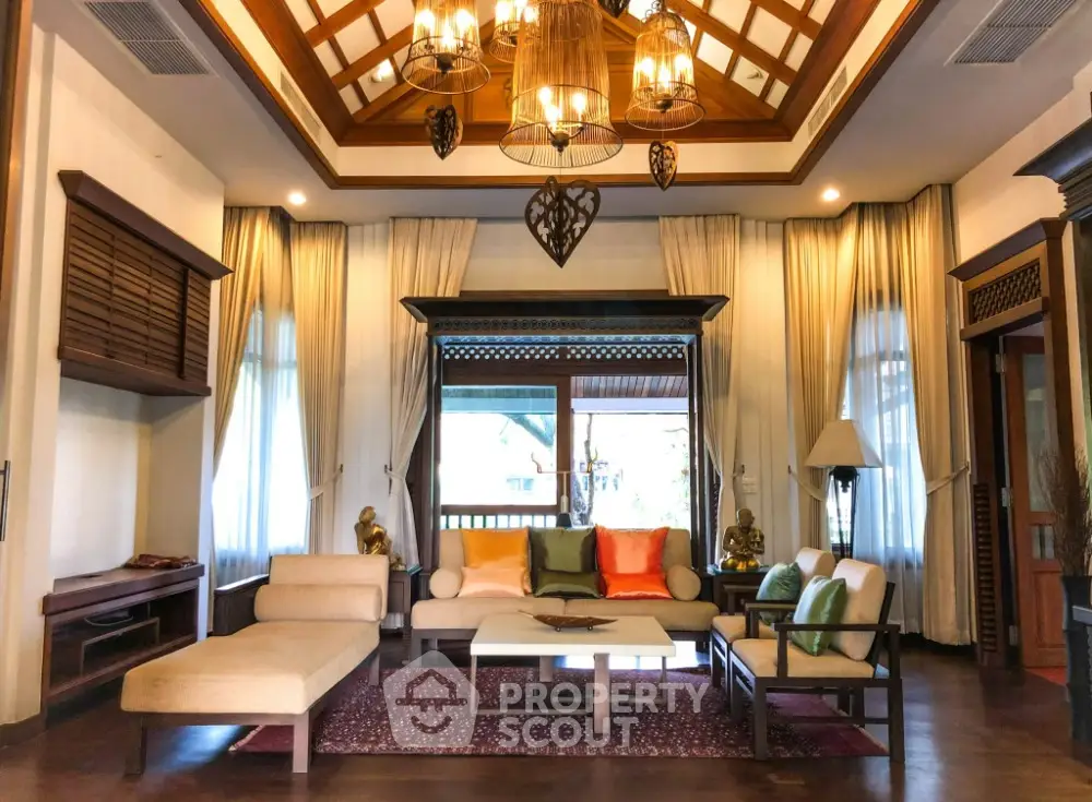 Luxurious living room with high ceiling, elegant chandelier, and plush seating, framed by rich wooden accents and warm lighting.