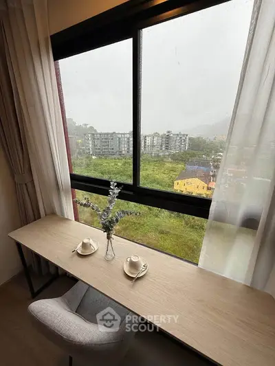 Cozy study nook with a view of lush greenery and distant buildings through a large window.