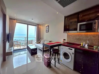 Modern open-plan living room with ocean view and balcony, featuring a compact kitchen and washing machine.