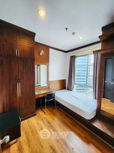 Cozy bedroom with wooden flooring, built-in wardrobe, and large window with city view.