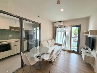 Modern living room with open kitchen, stylish furniture, and large windows offering natural light.