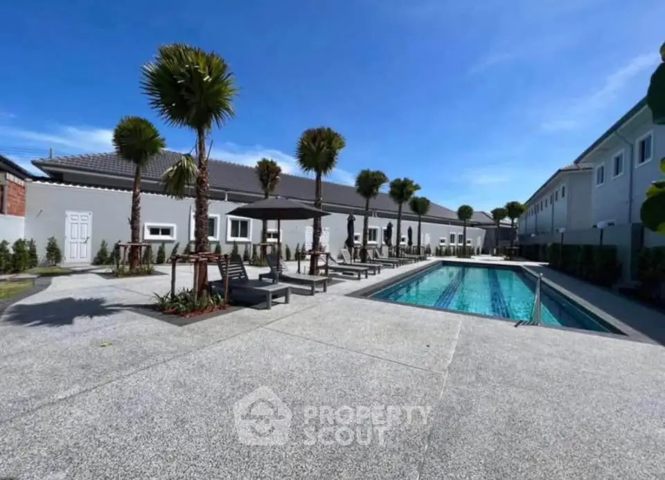 Luxurious residential complex with a pristine swimming pool and palm trees under a clear blue sky.