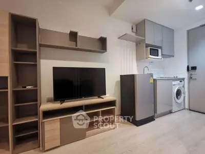 Modern apartment interior with TV, washing machine, and compact kitchen setup.