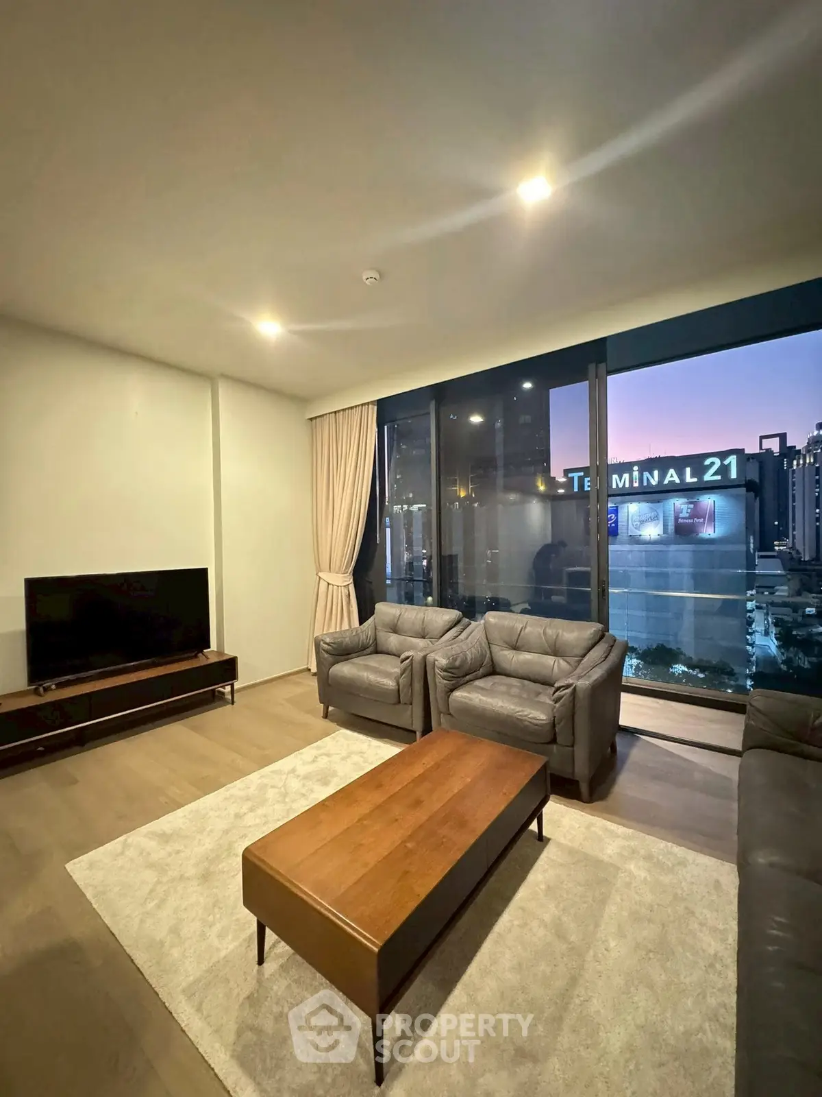Modern living room with city view near Terminal 21, featuring elegant furniture and large windows.