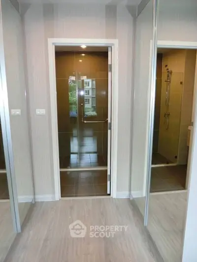 Modern bathroom with glass shower door and mirrored closet in stylish apartment.