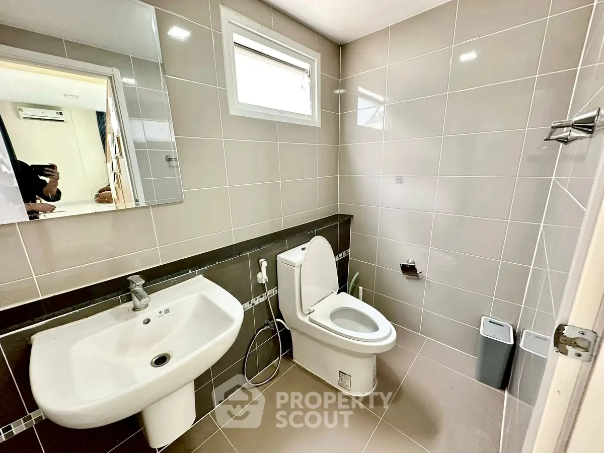 Modern bathroom with sleek fixtures and neutral tiles, featuring a large mirror and window for natural light.
