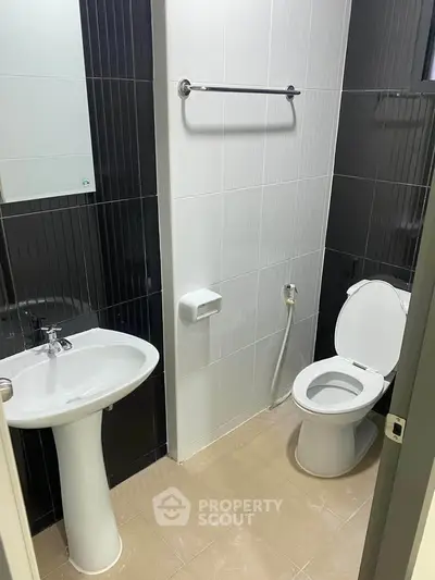 Modern bathroom with sleek black and white tiles, featuring a pedestal sink and toilet.