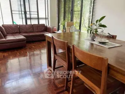 Spacious living room with wooden flooring and large windows, featuring a cozy leather sofa and elegant dining table.