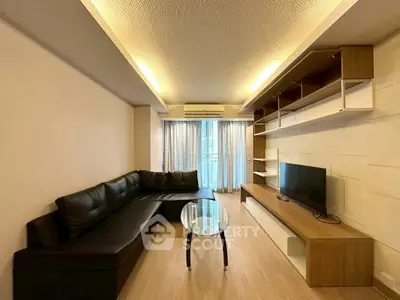 Modern living room with sleek black sofa, glass coffee table, and built-in TV unit, featuring ambient lighting.