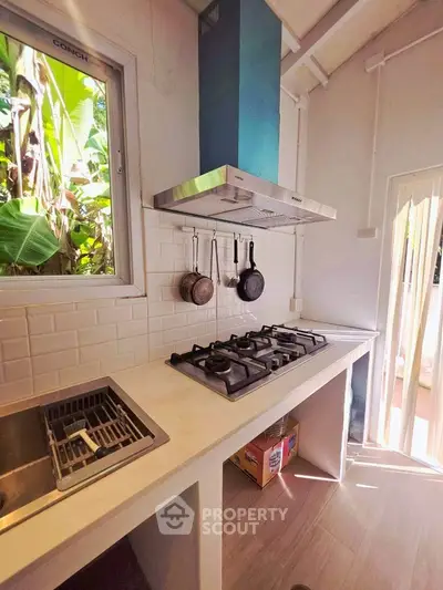 Modern kitchen with gas stove and sleek white countertops, featuring natural light and lush outdoor view.