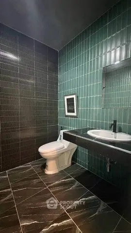 Modern bathroom with sleek black and green tiles, featuring a stylish sink and toilet.