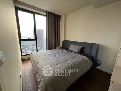 Modern bedroom with large window and city view, featuring a cozy bed and elegant decor.