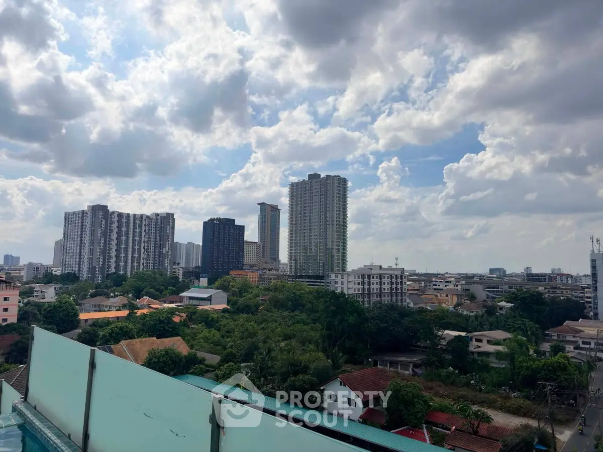 Stunning cityscape view from a rooftop with lush greenery and modern high-rise buildings under a cloudy sky.