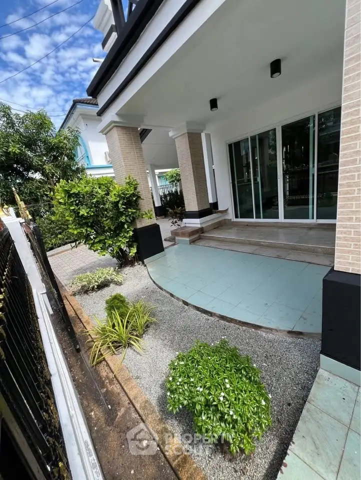 Charming residential entrance with lush garden and modern architecture, perfect for serene living.