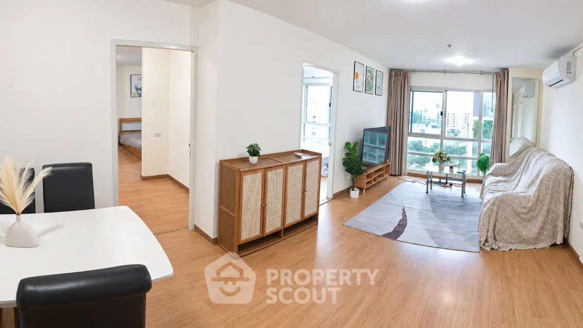Spacious modern living room with wooden flooring and large windows offering city views.