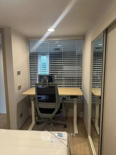 Modern study room with ergonomic chair and desk, featuring large window with blinds and mirrored closet doors.