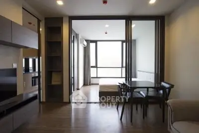 Modern open-plan living room with dining area and bedroom, featuring sleek furniture and large windows.