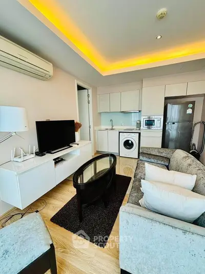 Modern living room with open kitchen, featuring sleek appliances and cozy seating area.