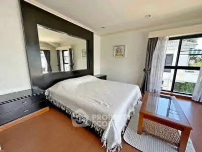 Spacious bedroom with large mirror and natural light, perfect for relaxation.