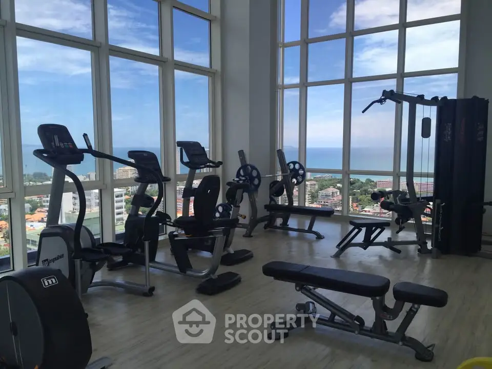 Spacious gym with panoramic city and ocean views, featuring modern exercise equipment.