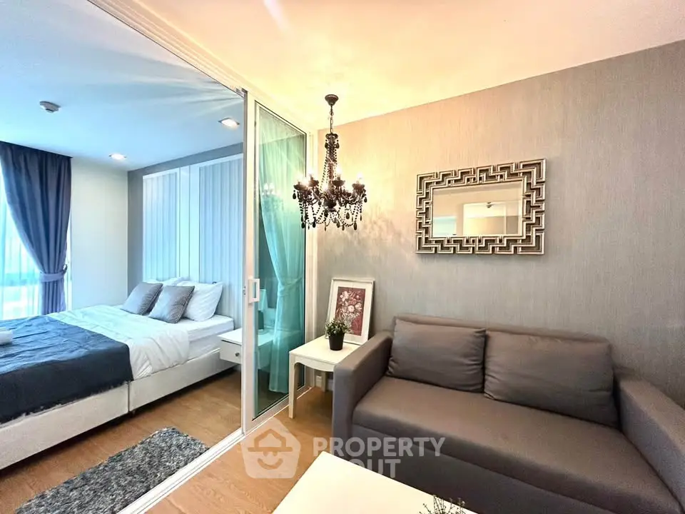 Modern living room with elegant chandelier and cozy bedroom separated by glass partition.