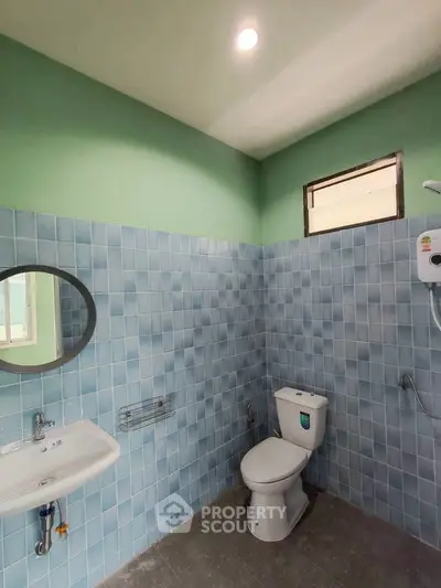 Modern bathroom with blue tiles and green walls, featuring a round mirror and shower heater.