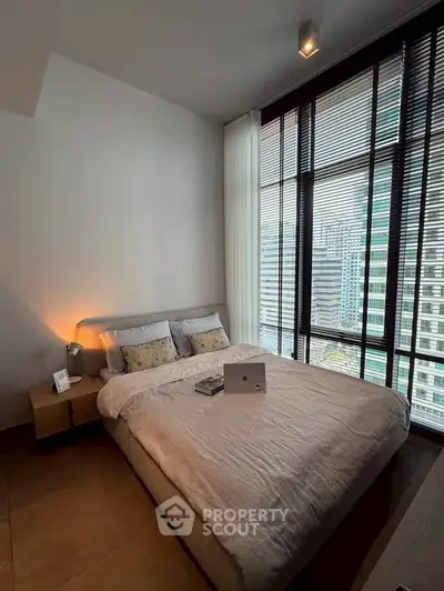 Modern bedroom with large windows offering city views, featuring a cozy bed and stylish decor.